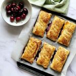 Cherry Pastry pies on a tray with cherries in a bowl next to it